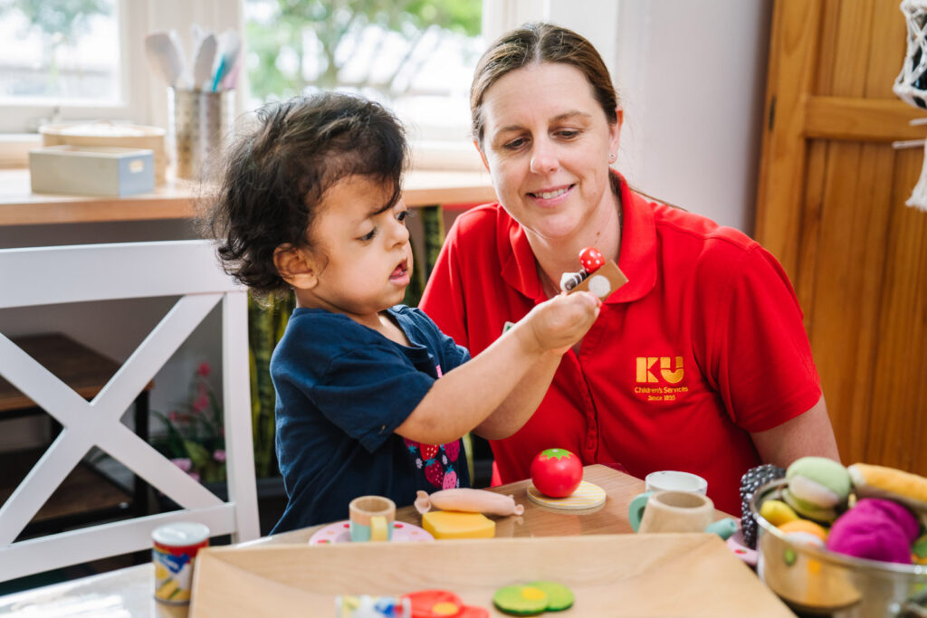 KU Briar Cottage childcare educator and a child playing with a kitchen set