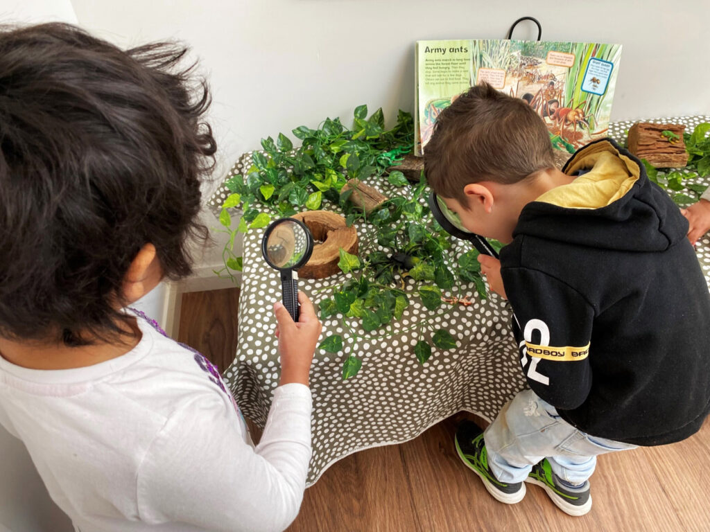 Children using magnifying glasses to look at objects at KU Ashmont childcare