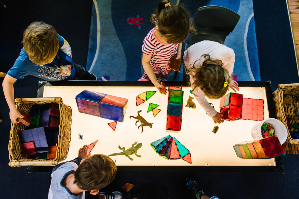 Children building with translucent shapes on a lightbox at KU Phoenix childcare