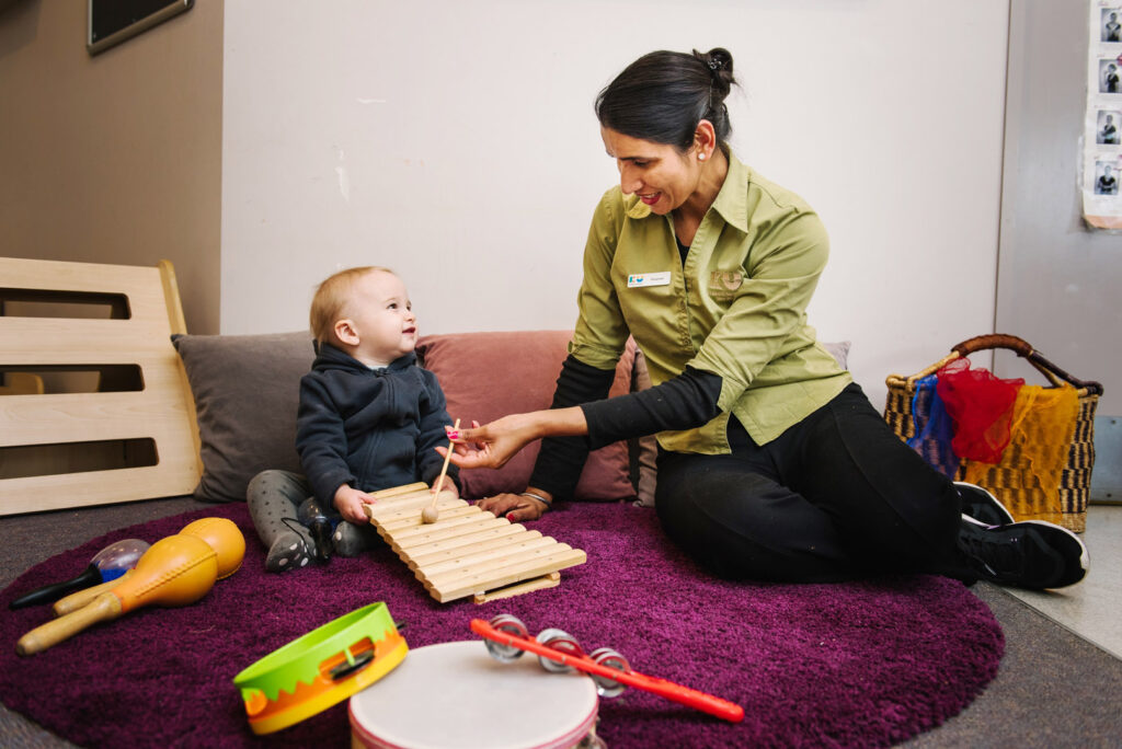 KU Village Green childcare educator and a child playing musical instruments