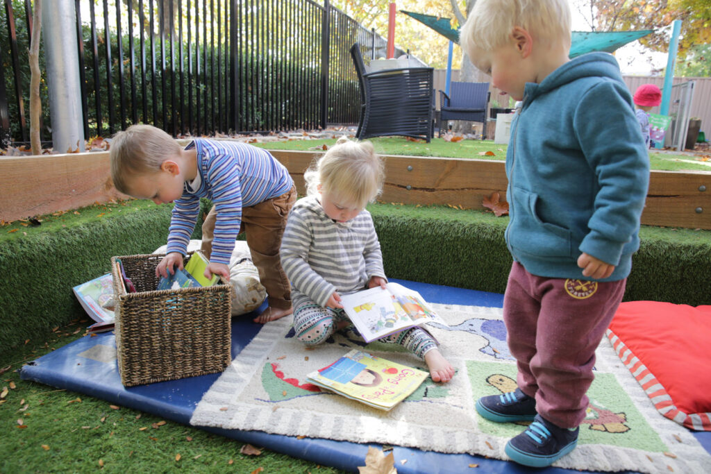 Children reading books outdoors at KU Braddon childcare