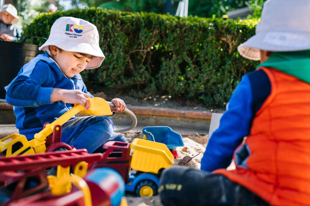 Children playing with trucks in the sand at KU Cabramatta AMEP childcare