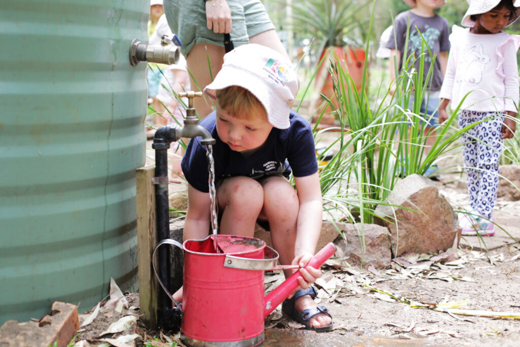 A child filling up a watering can at Kooinda Workbase Childcare