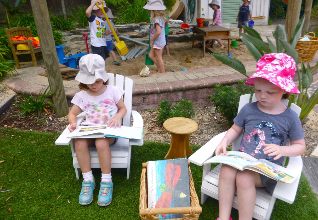 Children reading books outdoors at KU Castlecrag childcare