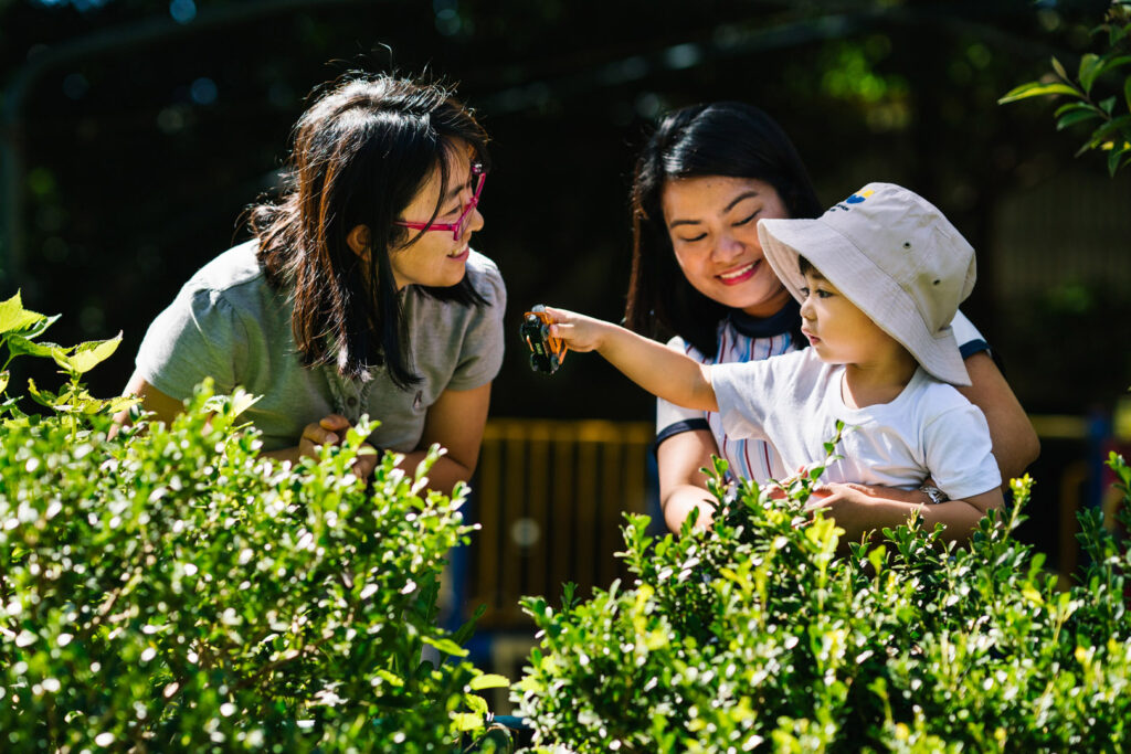 KU Chatswood Community childcare educators and a child playing in the garden