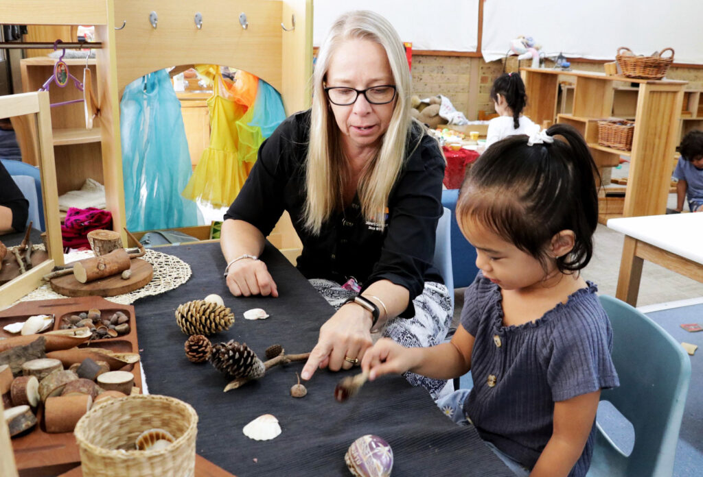 KU Chatswood Community childcare educator and a child studying some pine cones