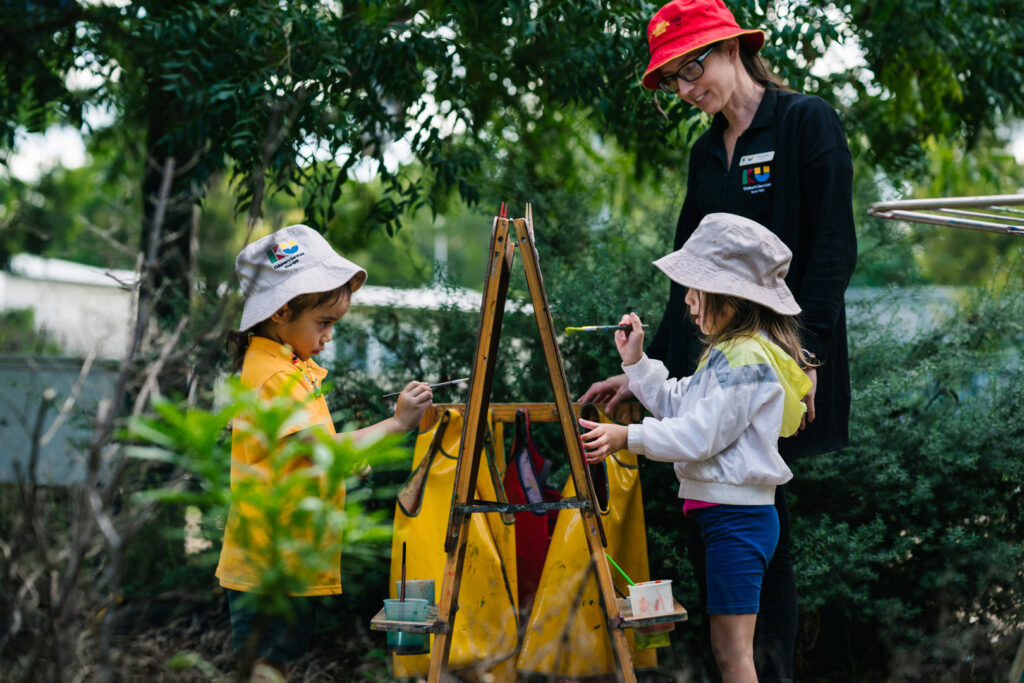 KU Hebersham childcare educator supervising some children painting outdoors