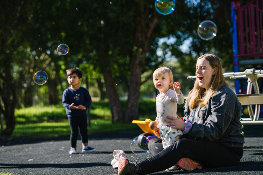 KU NSP Jesmond Neighbourhood childcare educator blowing bubbles with a child