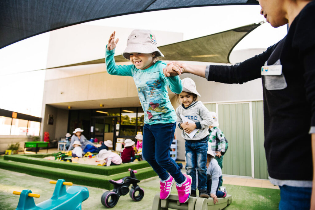 KU Liverpool AMEP childcare educator assisting children on the outdoor equipment at KU Liverpool AMEP childcare