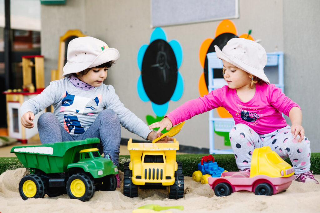 Children playing with trucks in the sand at KU Liverpool AMEP childcare