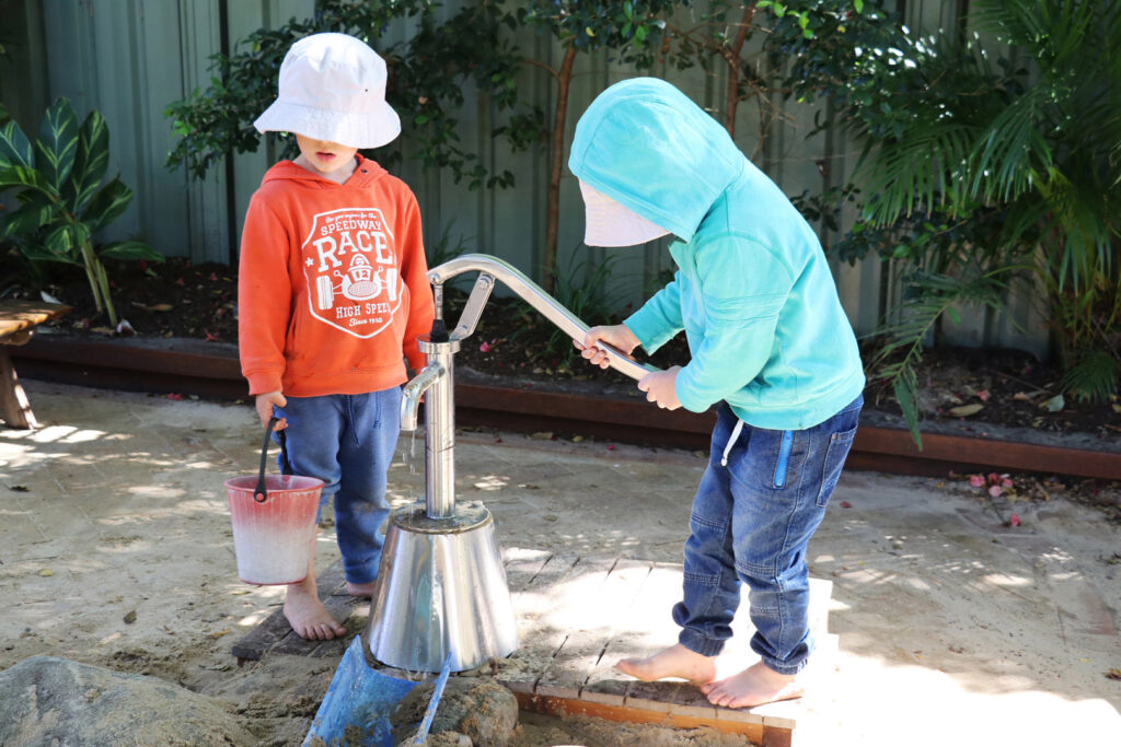 Children playing with a water pump at KU Newport childcare