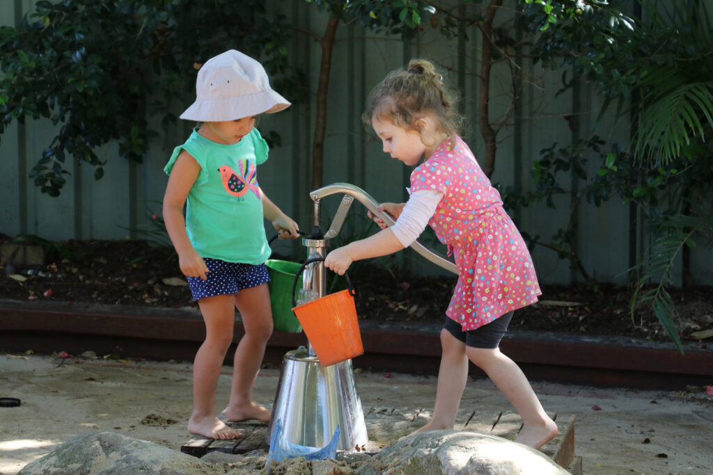 Children playing with a water pump at KU Newport childcare