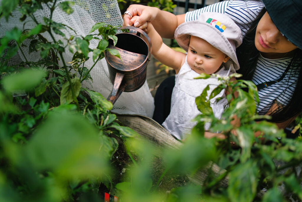 KU Carillon Avenue childcare educator helping a child water plants