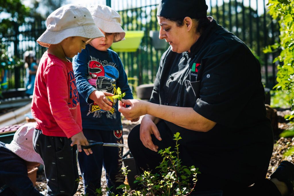 KU Playford Park childcare educator and children studying a plant