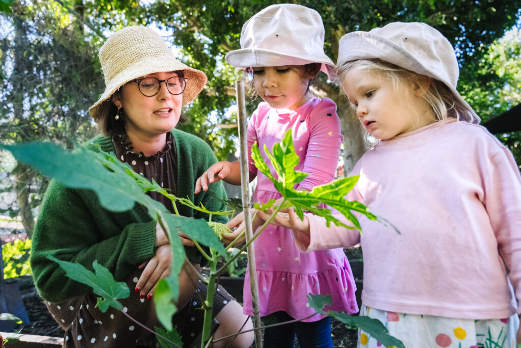 KU Petersham childcare educator and children studying a plant