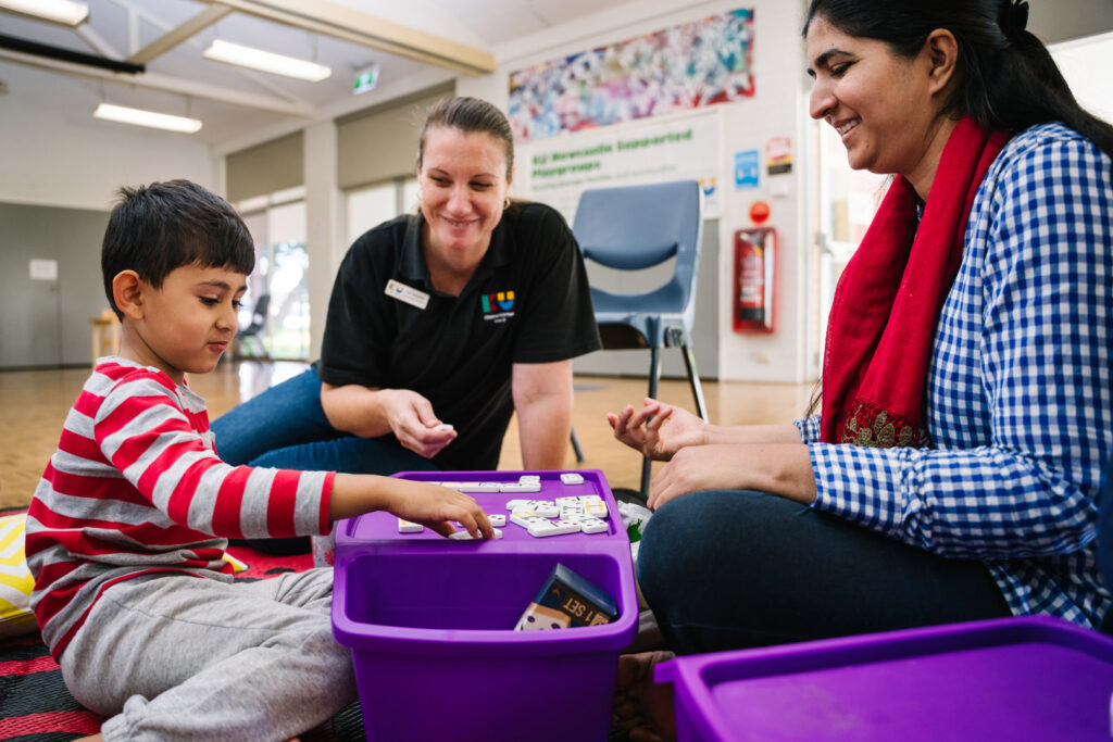 KU NSP Shortland Public School childcare educators and a child playing dominos