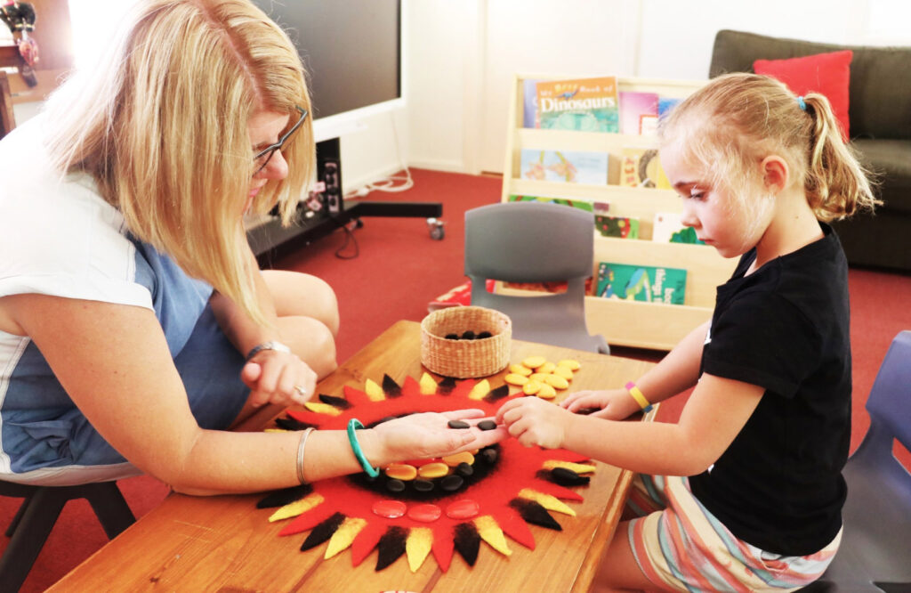 KU Kingfisher childcare educator and a child making a pattern out of rocks